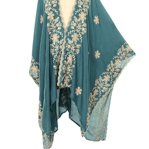 May include: Teal-colored embroidered kimono with a flowing design. The kimono features intricate floral embroidery in a contrasting beige color along the edges, neckline, and sleeves. The garment is displayed on a mannequin against a white background.
