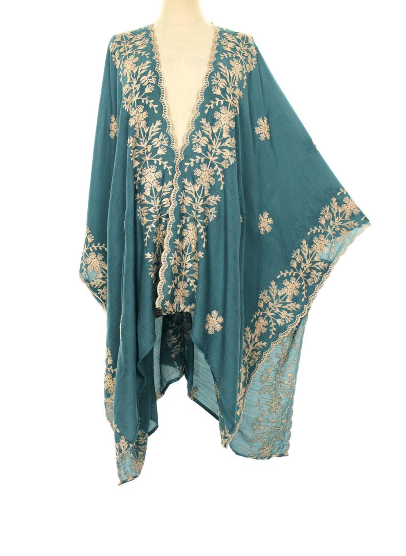 May include: Teal-colored embroidered kimono with a flowing design. The kimono features intricate floral embroidery in a contrasting beige color along the edges, neckline, and sleeves. The garment is displayed on a mannequin against a white background.