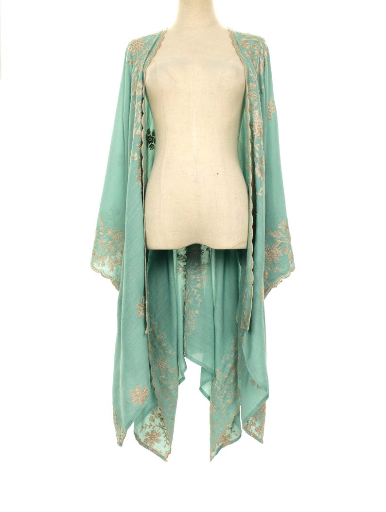 May include: A flowing, mint green kimono-style garment with intricate gold embroidery along the edges and sleeves. The lightweight fabric drapes elegantly, creating a relaxed silhouette. The embroidery features floral and geometric patterns.