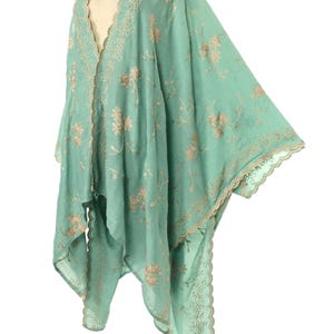 May include: A flowing, mint green kimono-style garment with intricate floral embroidery in a contrasting beige color. The edges are finished with a delicate, scalloped trim. The lightweight fabric drapes elegantly, suggesting a bohemian or vintage aesthetic.
