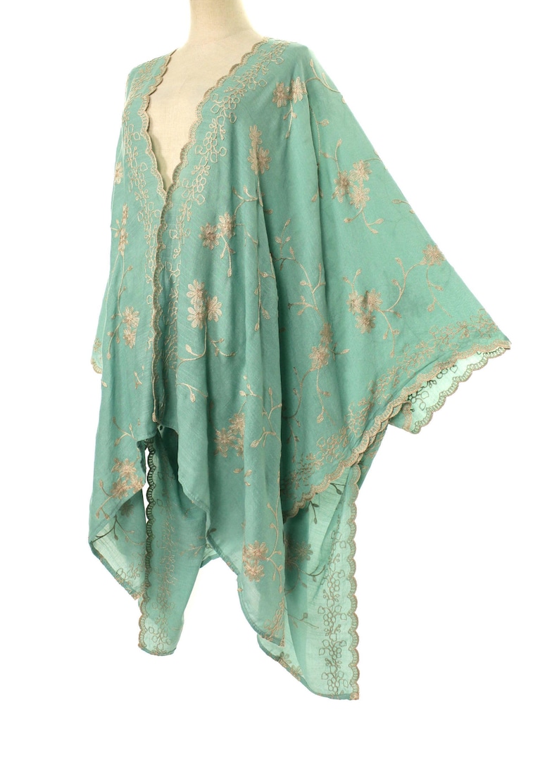 May include: A flowing, mint green kimono-style garment with intricate floral embroidery in a contrasting beige color. The edges are finished with a delicate, scalloped trim. The lightweight fabric drapes elegantly, suggesting a bohemian or vintage aesthetic.
