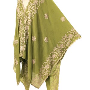 May include: Olive green embroidered cape with a V-neckline. The cape features intricate floral embroidery in a contrasting light beige color along the edges and around the neckline. The fabric appears lightweight and flowing, suitable for layering.