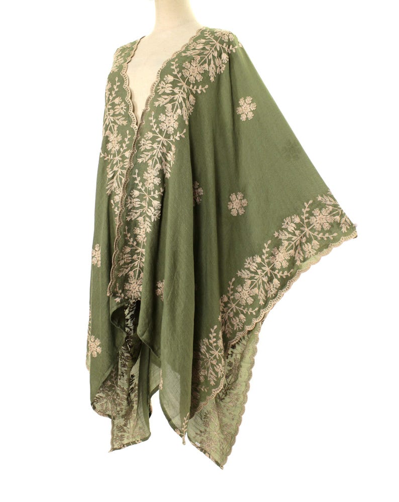 May include: Olive green embroidered shawl with floral and leaf patterns. The shawl features a scalloped edge and intricate beige embroidery along the borders and neckline. The lightweight fabric drapes elegantly, showcasing the detailed design.