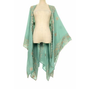 May include: A light teal kimono-style garment with intricate gold embroidery along the edges and sleeves. The open-front design drapes elegantly, showcasing a flowing silhouette. The garment is displayed on a mannequin.