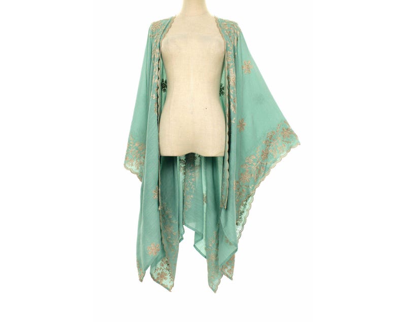 May include: A light teal kimono-style garment with intricate gold embroidery along the edges and sleeves. The open-front design drapes elegantly, showcasing a flowing silhouette. The garment is displayed on a mannequin.