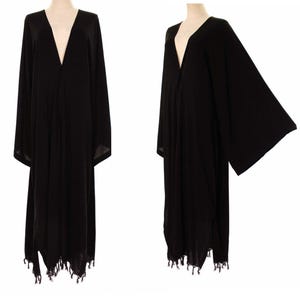 May include: A long, black kimono-style robe with a deep V-neck and wide sleeves. The robe has a fringed hemline and is displayed on a mannequin. The fabric appears lightweight and flowing, suitable for layering.