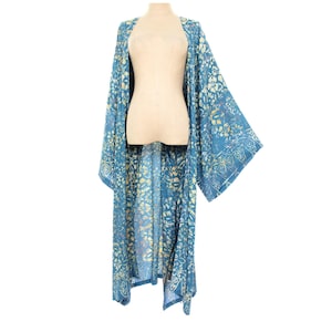 May include: A long, flowing blue kimono with a floral pattern in shades of yellow and white. The kimono is displayed on a mannequin, showcasing its open front and wide sleeves. The fabric appears lightweight and suitable for layering.