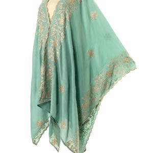 May include: A flowing, seafoam green shawl with intricate, embroidered floral patterns in a contrasting tan color. The shawl has a V-neck design and scalloped edges, creating a delicate and elegant look. The fabric appears lightweight and airy.