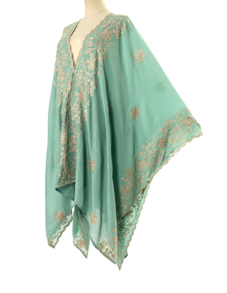 May include: A flowing, seafoam green shawl with intricate, embroidered floral patterns in a contrasting tan color. The shawl has a V-neck design and scalloped edges, creating a delicate and elegant look. The fabric appears lightweight and airy.