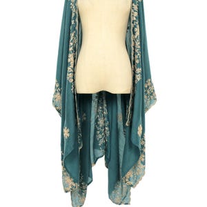 May include: Teal-colored embroidered kimono-style wrap. The wrap features intricate floral embroidery in a contrasting light beige color along the edges and front panels. The garment is draped over a mannequin, showcasing its flowing design.