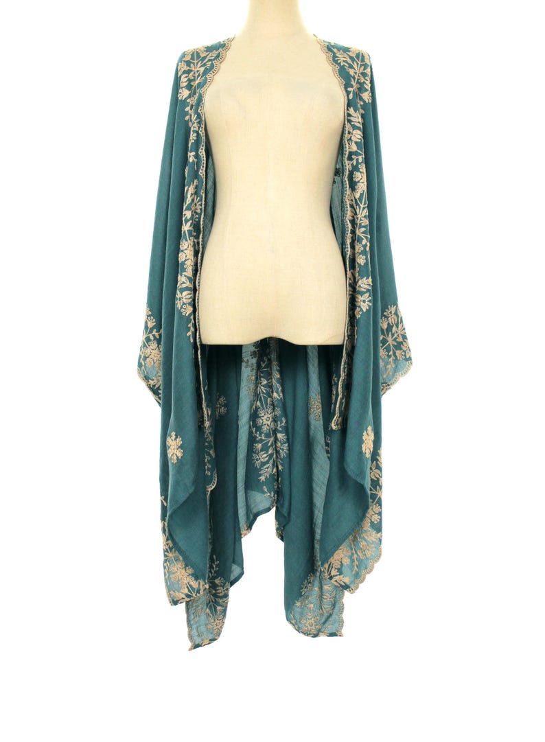 May include: Teal-colored embroidered kimono-style wrap. The wrap features intricate floral embroidery in a contrasting light beige color along the edges and front panels. The garment is draped over a mannequin, showcasing its flowing design.