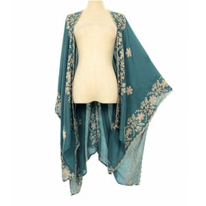 May include: Teal-colored embroidered kimono-style wrap. The wrap features intricate floral embroidery in a contrasting light beige thread along the edges and front. The garment is displayed on a mannequin, showcasing its flowing design.