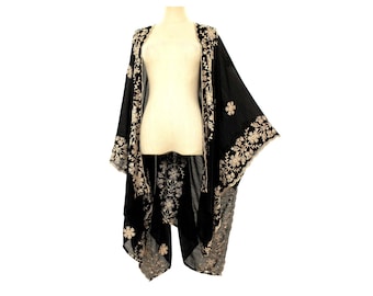 May include: Black kimono-style cover-up with floral embroidery in cream. The open-front design features wide sleeves and a flowing silhouette. The embroidery is detailed along the edges and on the back, creating a bohemian aesthetic.