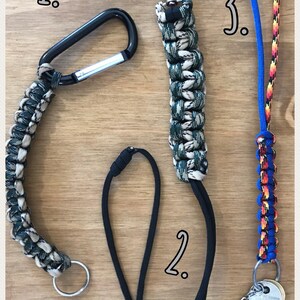 May include: Three keychains with different styles. The first keychain is made of black and white paracord with a silver carabiner. The second keychain is made of black paracord. The third keychain is made of blue, red, and yellow paracord with a silver key ring and a purple Lego brick.