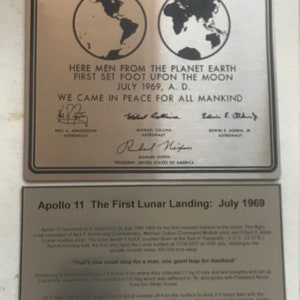 Puede incluir: Una placa de plata que conmemora el alunizaje del Apolo 11 con el texto "Here men from the planet Earth first set foot upon the Moon July 1969, A.D. We came in peace for all mankind." La placa incluye las firmas de Neil Armstrong, Michael Collins y Edwin E. Aldrin Jr., así como del presidente Richard Nixon. Una placa más pequeña debajo dice "Apollo 11 The First Lunar Landing: July 1969" y proporciona una breve descripción de la misión.
