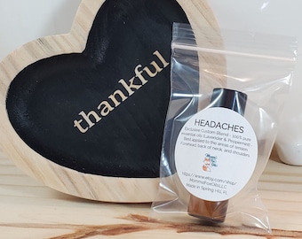 May include: A small clear glass bottle with a black cap containing essential oil blend for headaches. The bottle is in a clear plastic bag with a white label that reads "HEADACHES Exclusive Custom Blend - 100% pure essential oils (Lavender & Peppermint) - Best applied to the areas of tension. Forehead, back of neck, and shoulders. https://www.etsy.com/shop/MommaFoxOilsLLC Made in Spring Hill FL"
