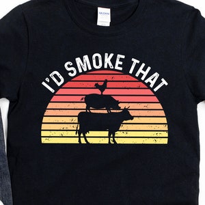 May include: Black t-shirt with a retro sunset graphic and the text "I'd Smoke That". The graphic features a cow, pig, and chicken stacked on top of each other.