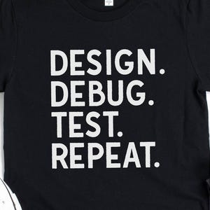 May include: Black t-shirt with the words "DESIGN. DEBUG. TEST. REPEAT." in white, alongside dark grey jeans and white canvas trainers. A casual outfit suitable for everyday wear.