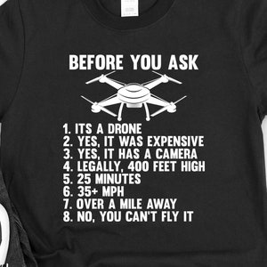 May include: Black t-shirt with white text that reads "Before You Ask" and a drone graphic. The text lists facts about drones, including that they are expensive, have cameras, and can fly up to 400 feet high.