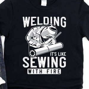 May include: Black t-shirt with a white graphic of a welder and the text "Welding It's Like Sewing With Fire".