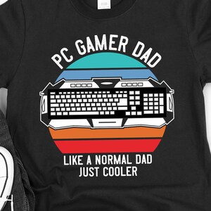 May include: Black t-shirt with a retro-style graphic that says "PC Gamer Dad" with a keyboard and sunset design. The text below the graphic says "Like a normal dad just cooler."