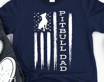 Könnte beinhalten: Ein marineblaues T-Shirt mit einem weißen amerikanischen Flaggen-Design, das die Silhouette eines Pitbull-Hundes zeigt. Der Text "Pitbull Dad" ist vertikal auf der Flagge geschrieben.