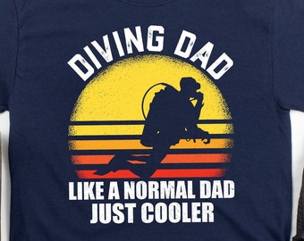 Op de afbeelding: Donkerblauw T-shirt met een retro zonsondergang afbeelding en de tekst "Diving Dad Like a Normal Dad Just Cooler".