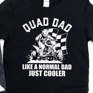 May include: Black t-shirt with a white graphic of a person riding an ATV with the text "QUAD DAD LIKE A NORMAL DAD JUST COOLER".