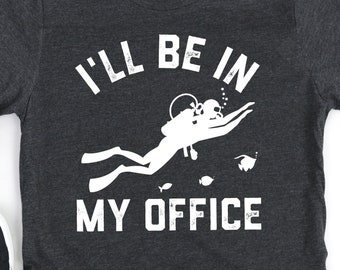 Puede incluir: Camiseta gris oscuro con el texto blanco "I'll Be In My Office" y un gráfico de buzo. Zapatillas negras con suelas blancas a la izquierda. La camiseta es de cuello redondo y está hecha de un material suave.
