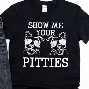 Pode incluir: Camiseta preta com texto branco que diz "Show Me Your Pitties" e um gráfico de dois cães pit bull usando óculos de sol.