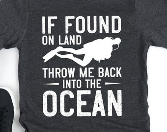 Könnte beinhalten: Ein dunkelgraues T-Shirt mit einer weißen Grafik, auf der "Wenn gefunden an Land, werfe mich zurück ins Meer" steht. Die Grafik enthält auch eine Silhouette eines Tauchers.
