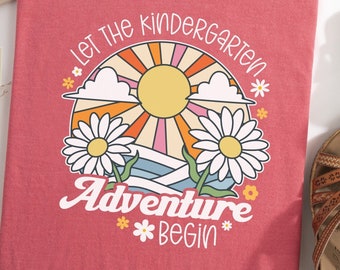 May include: A red t-shirt with a graphic design of a sun, clouds, and flowers. The text "Let the Kindergarten Adventure Begin" is printed on the shirt.