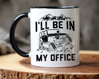 Puede incluir: Taza de café de cerámica blanca con asa negra y borde negro. La taza tiene un gráfico en blanco y negro de un jeep conduciendo por montañas con el texto "I'll be in my office".