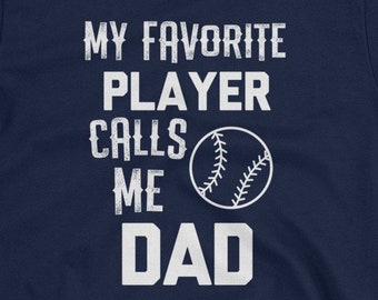 May include: Navy blue t-shirt with white text that reads "My favorite player calls me dad" and a white baseball graphic.