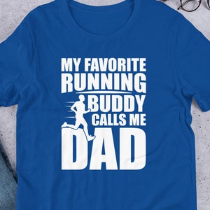 Könnte beinhalten: T-Shirt in Royalblau mit weißem Text, der "Mein Lieblingslaufkumpel nennt mich Papa" lautet. Neben dem Text ist eine laufende Figur abgebildet.