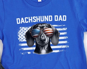 May include: Blue t-shirt with the text "Dachshund Dad" and a cartoon dachshund wearing sunglasses and an American flag bandana.