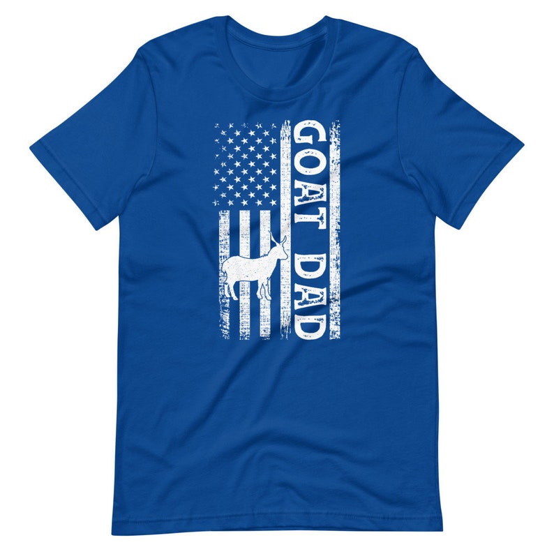以下が含まれることがあります： ロイヤルブルーのTシャツに、白のダメージ加工されたアメリカ国旗のデザインと、国旗の右側に縦に「GOAT DAD」という文字がプリントされています。