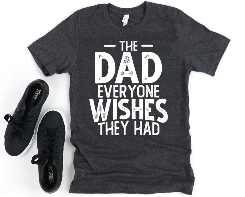 May include: A dark gray t-shirt with white text that reads "The Dad Everyone Wishes They Had".