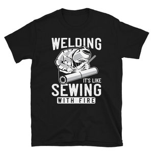 May include: Black t-shirt with a white graphic of a welder welding a pipe. The text "Welding It's Like Sewing With Fire" is printed on the shirt.
