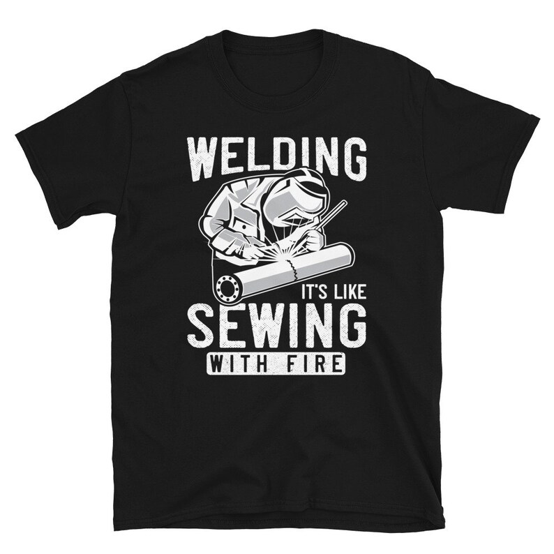 May include: Black t-shirt with a white graphic of a welder welding a pipe. The text "Welding It's Like Sewing With Fire" is printed on the shirt.