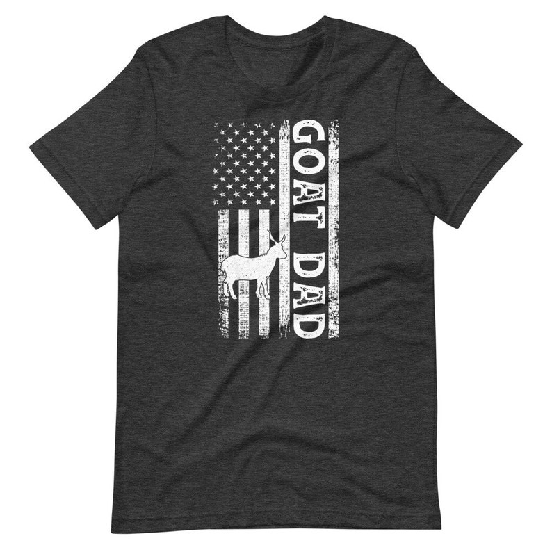 以下が含まれることがあります： 暗いヘザーグレーのTシャツに、使い古したアメリカ国旗のデザインが施されています。国旗には白いヤギのシルエットと白い文字で「GOAT DAD」と書いてあります。