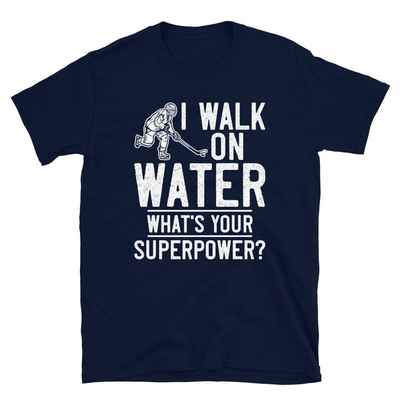 May include: A navy blue t-shirt with a white graphic of a hockey player skating on water. The text "I walk on water" and "What's your superpower?" is printed in white on the shirt.