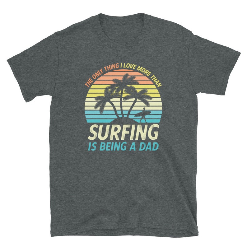 Pu&ograve; includere: Una maglietta grigio scuro melange con una grafica di tramonto con palme e un surfista. Il testo recita "L'unica cosa che amo pi&ugrave; del surf &egrave; essere pap&agrave;."