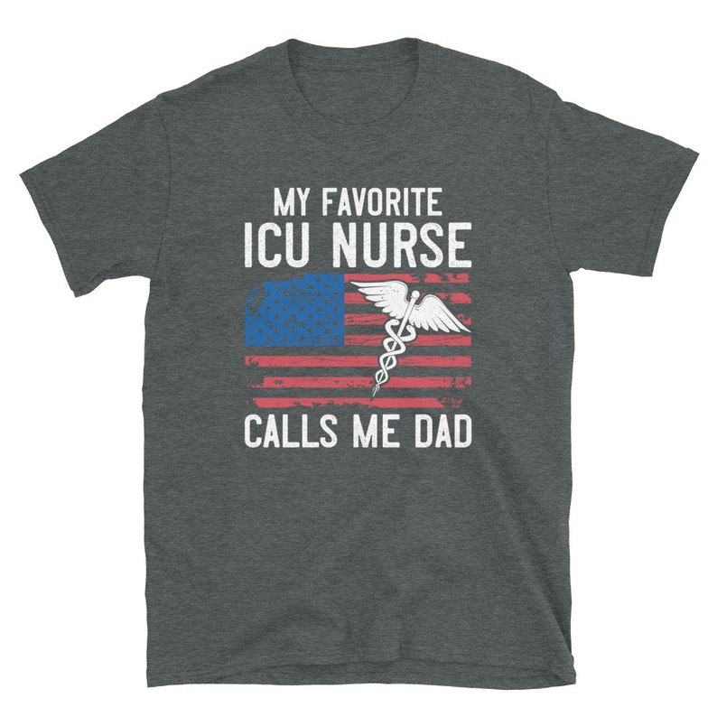 May include: A dark heather grey t-shirt with a white graphic design. The graphic features an American flag with a medical caduceus symbol and the text "My Favorite ICU Nurse Calls Me Dad".