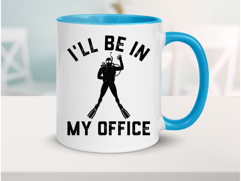Puede incluir: Taza de cer&aacute;mica blanca con interior y asa azules. La taza presenta el texto "I'LL BE IN MY OFFICE" en negro, junto con una silueta de un buceador. El buceador lleva una m&aacute;scara de buceo, aletas y un tanque.