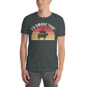 May include: A dark heather grey t-shirt with a vintage-style sunset graphic and the text "I'd Smoke That". The graphic features a pig, a cow, and a chicken stacked on top of each other.