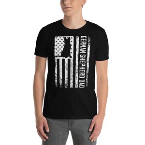 May include: Black t-shirt with a white distressed American flag design and a German Shepherd silhouette. The text "GERMAN SHEPHERD DAD" is printed vertically on the right side of the flag.