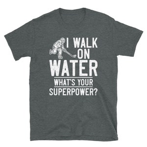 May include: A dark heather grey t-shirt with a white graphic of a hockey player skating on water. The text "I walk on water" is above the graphic and "What's your superpower?" is below the graphic.