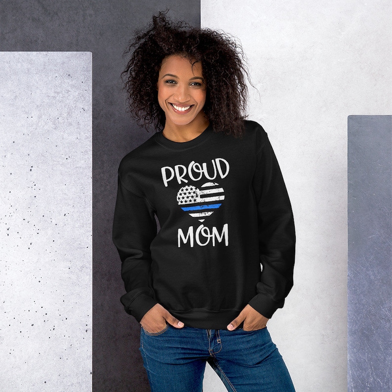 May include: Black sweatshirt with the words "PROUD MOM" in white. A heart-shaped design features the American flag with a blue line. The sweatshirt is a crew neck style.