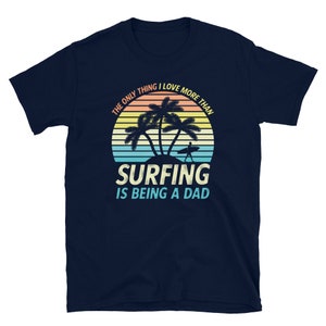 Pu&ograve; includere: T-shirt blu navy con una grafica di tramonto retr&ograve; con palme e un surfista. Il testo recita "L'unica cosa che amo pi&ugrave; del surf &egrave; essere pap&agrave;."